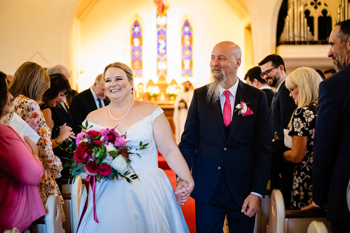 A joyful bride and groom holding hands while walking down the aisle of a church after their wedding ceremony