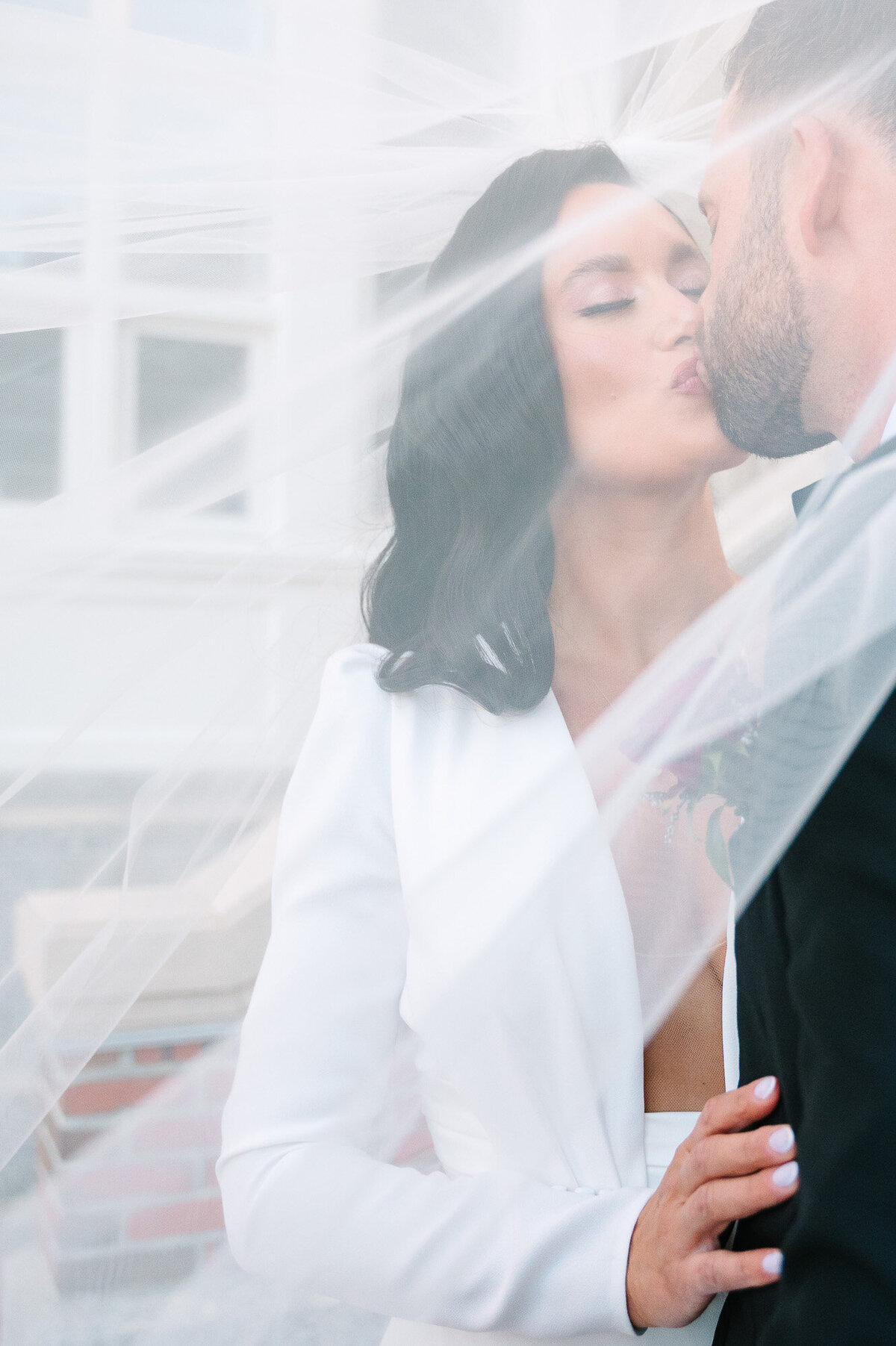bride and groom kissing while covered by veil