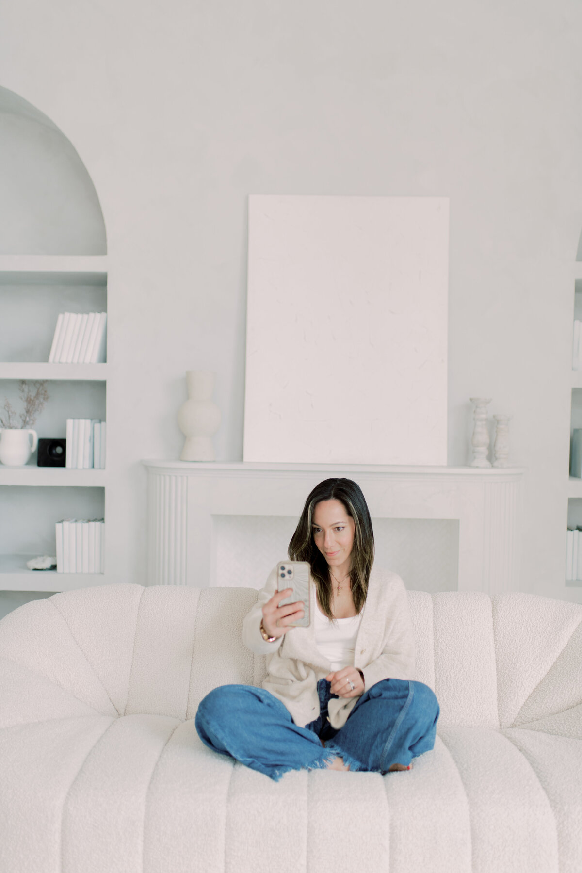 Portrait of a confident woman seated on a modern bench in a minimal white studio with phone in hand