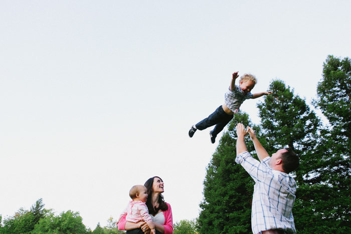 Candid shot of dad throwing child up in the air while mom and other child watch smiling