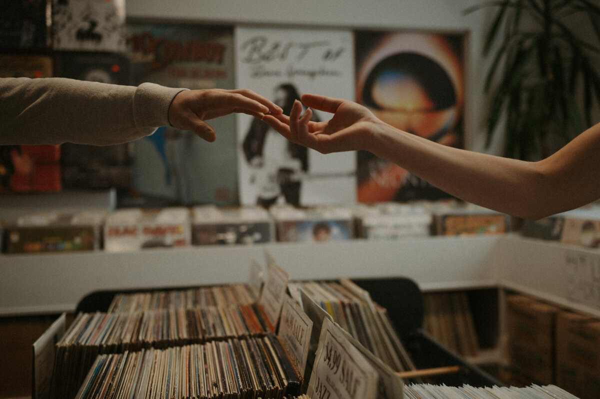 Photo of couples hands reaching across records at record store
