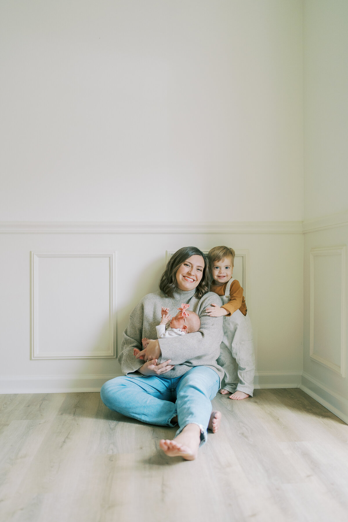 mom sitting on ground holding newborn baby and little boy