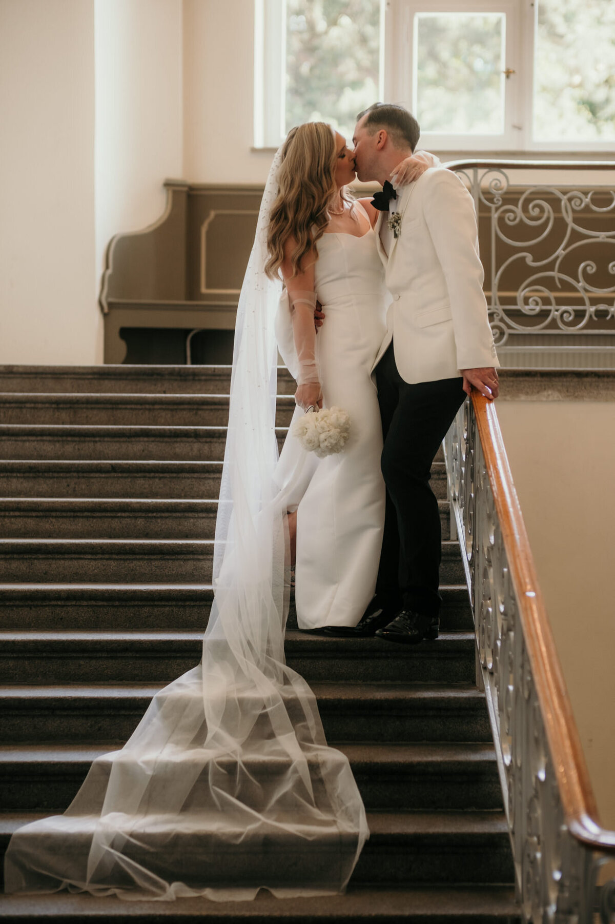 Auf einer Treppe im Gebäude stehend küsst sich das frisch verheiratete Paar.