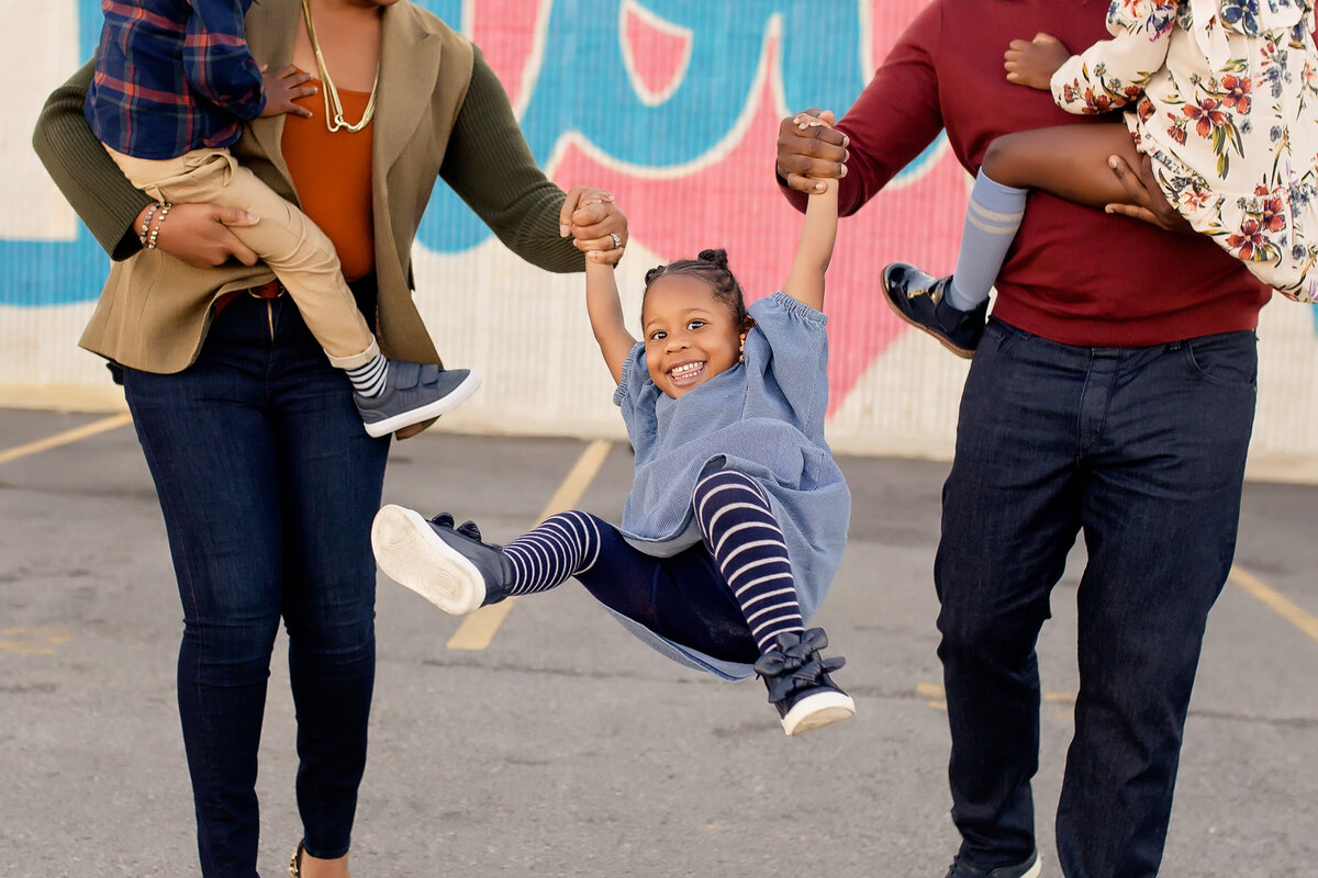 A family swings their daughter in an urban photo session.