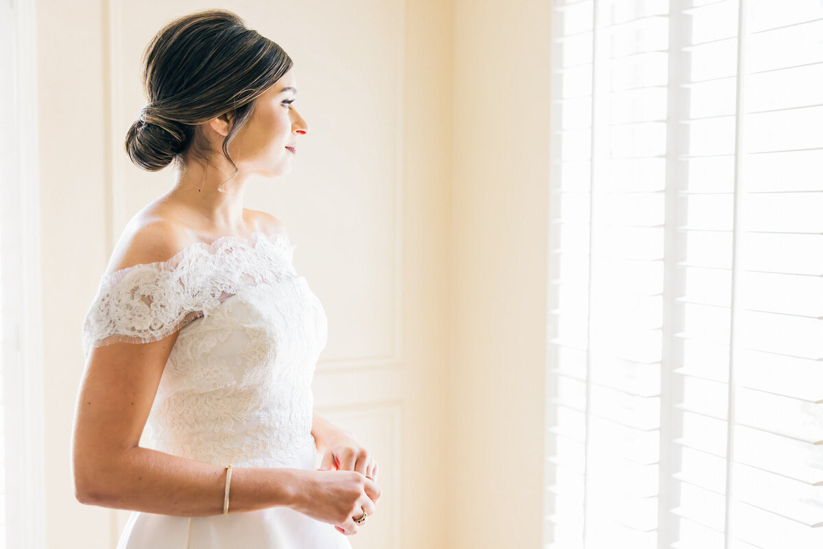 Bride, after getting ready, gazes longingly out the window, capturing a quiet, heartfelt moment of anticipation before walking down the aisle.