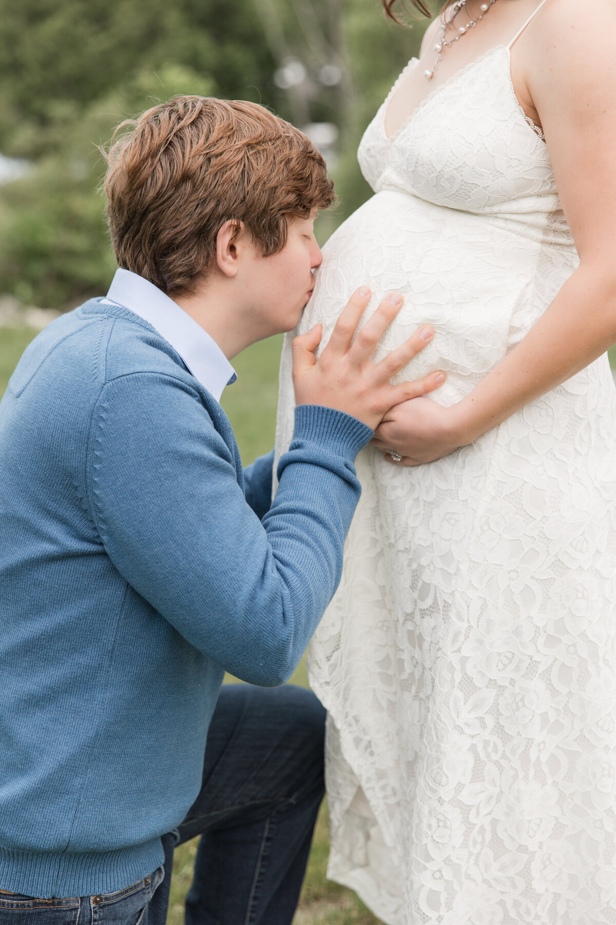 Expectant couple with father kneeling down and kissing the baby bump