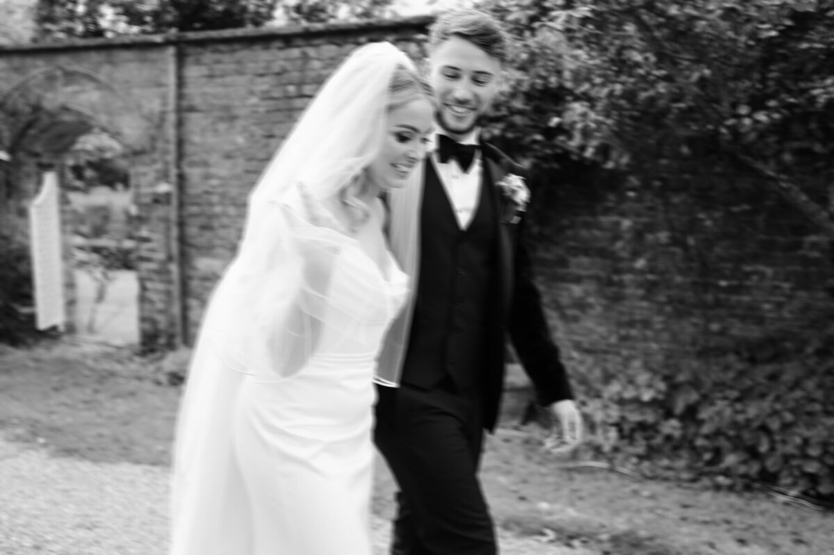 Blurry, documentary style image of a smiling bride and groom walking past the camera