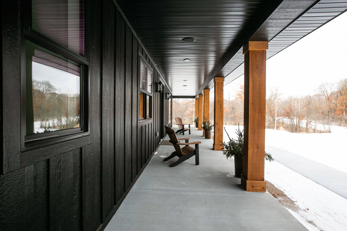 Exterior view of custom home in Elk River, Minnesota with black siding, wood details and front porch built by Cornerstone Custom Builds
