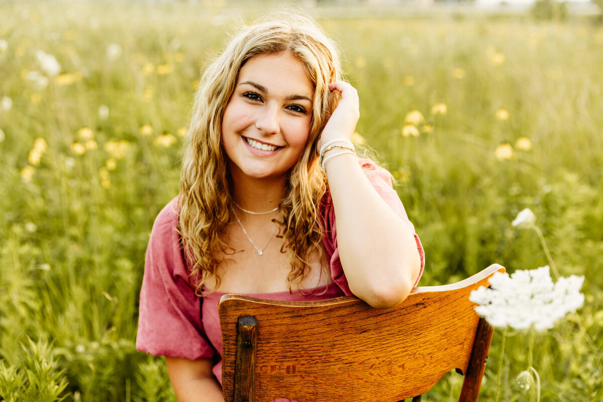 high school senior girl sitting in a chair in a field of flowers by Ashley Kalbus Photography