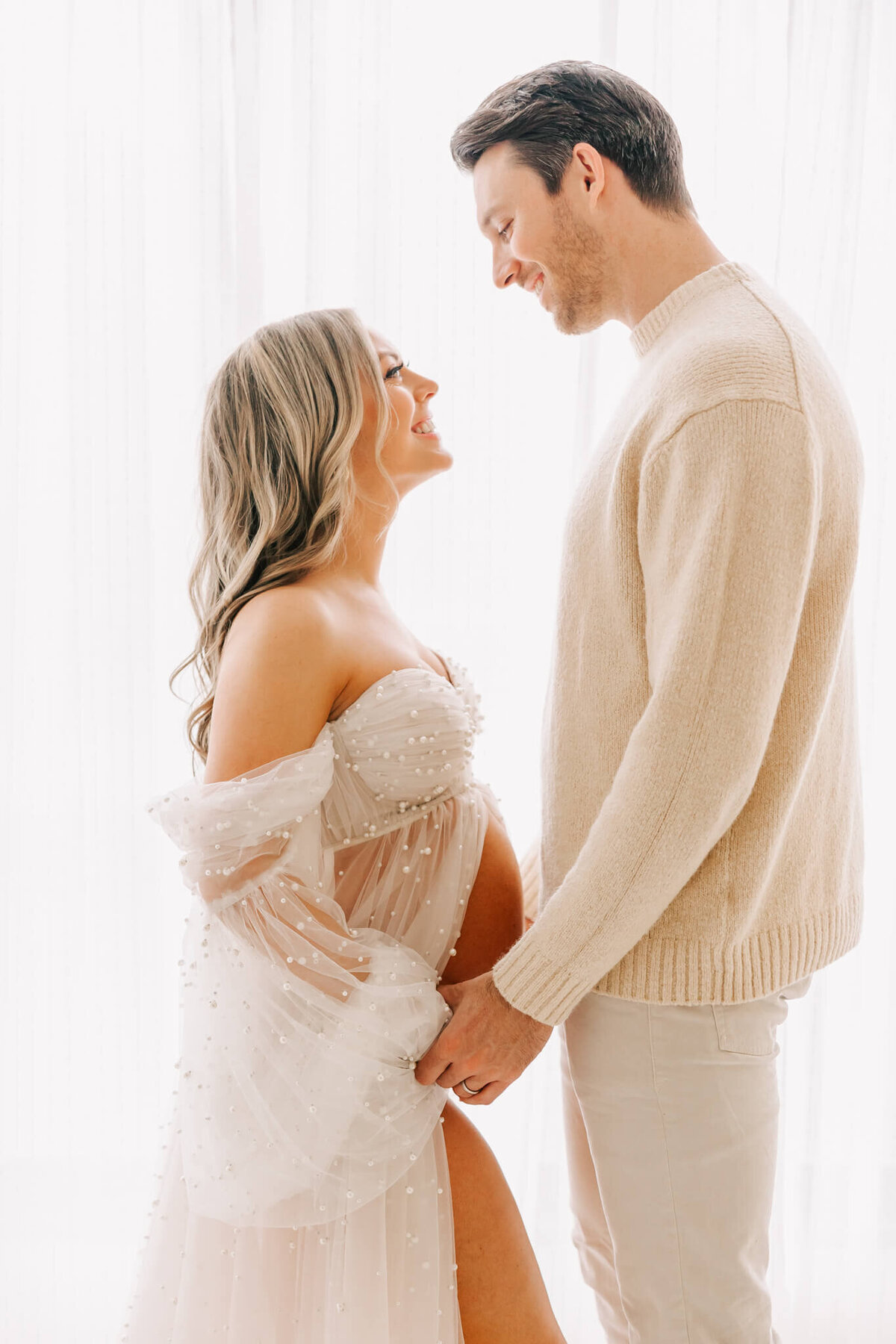 portrait of blonde woman looking at husband. they are both wearing cream and white and smiling at each other with joy