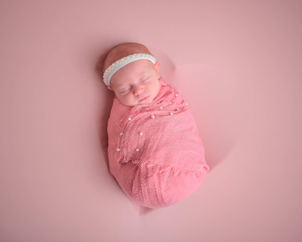 Kitsap in home photo session for newborn girl sleeping in a pink heart bowl.