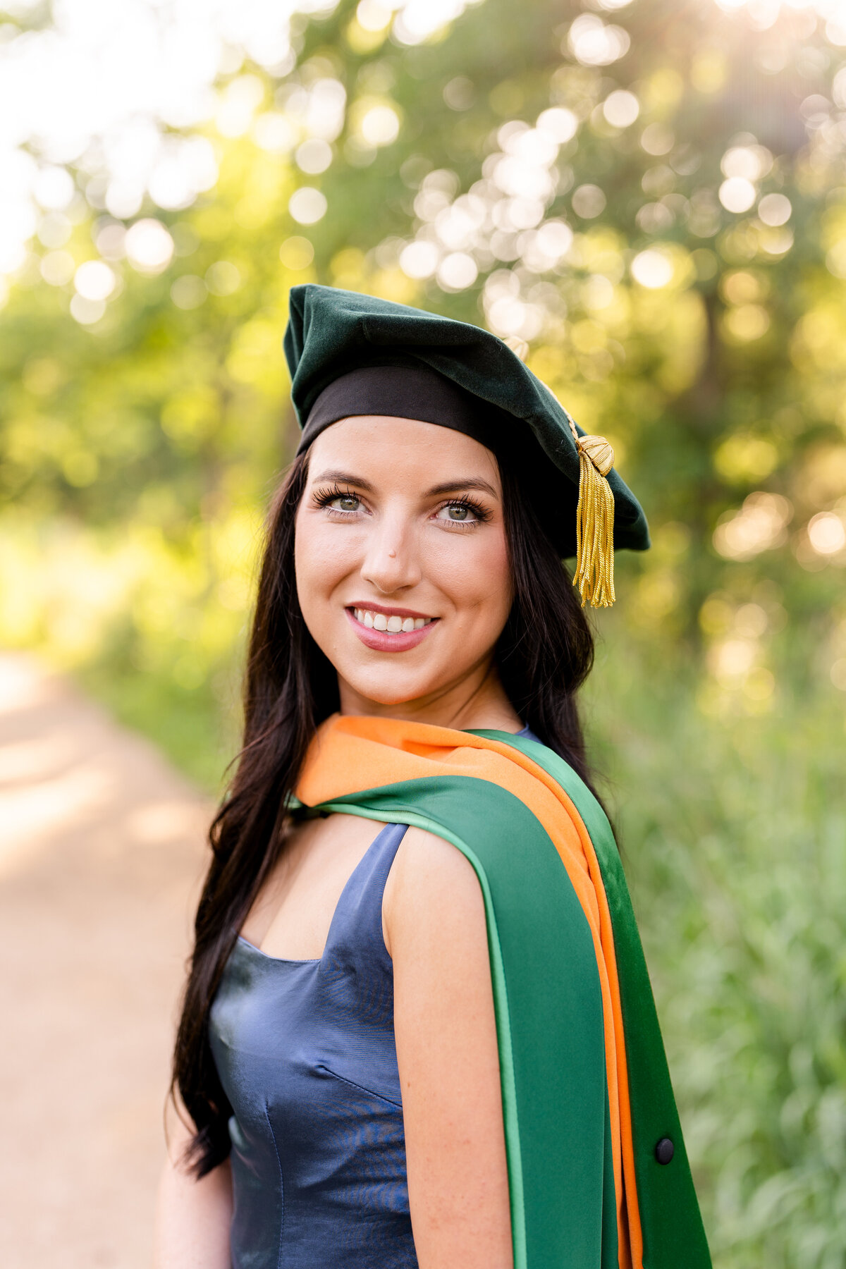Baylor senior girl smiling over shoulder while wearing doctoral hood and hat at the Houston Arboretum