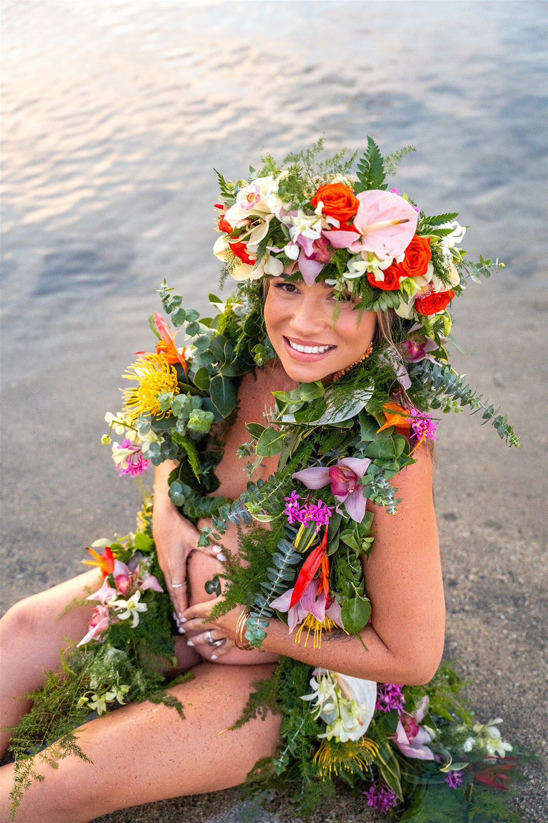Pregnant woman wearing leis and flowers sitting in the ocean, taken by big island family photographer