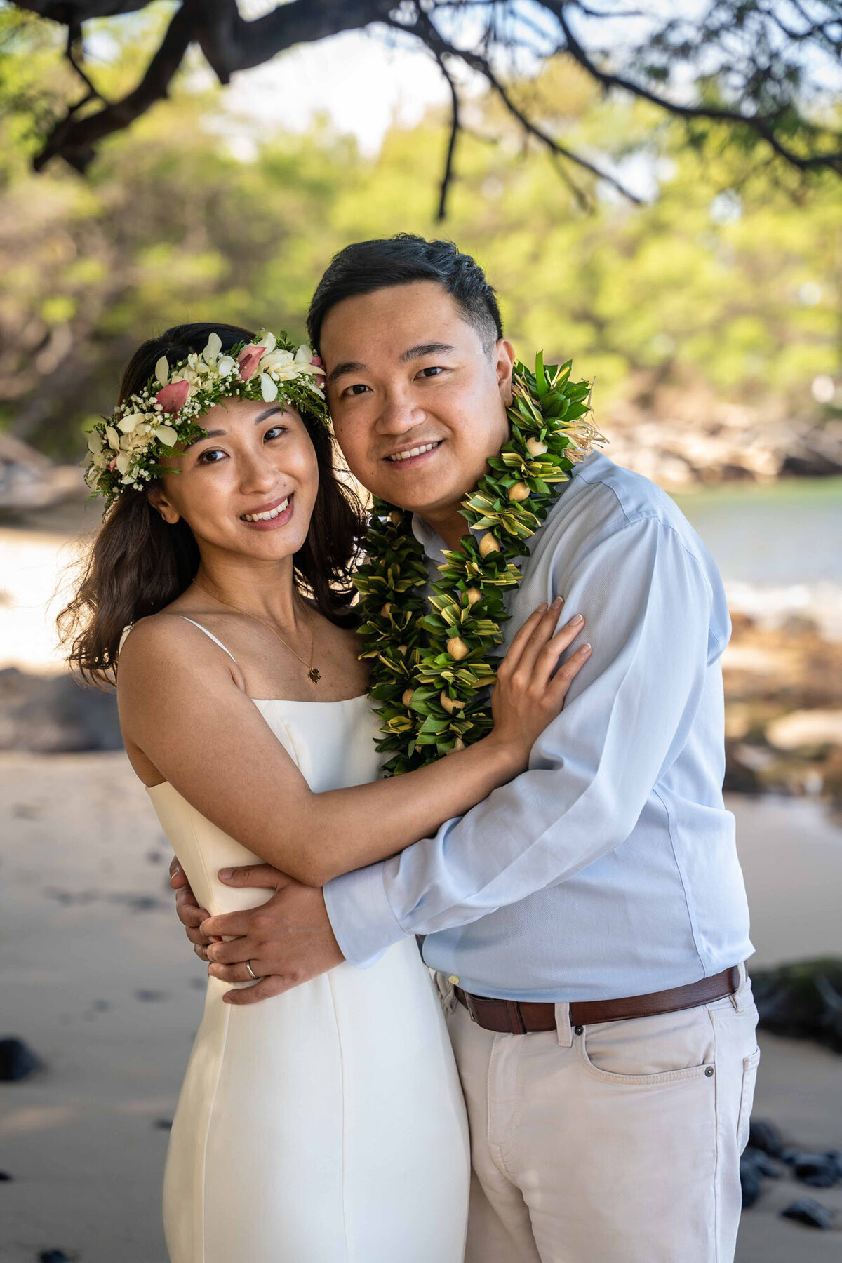 Couple smiling and wearing leis, posing for engagement photographer in Hawaii
