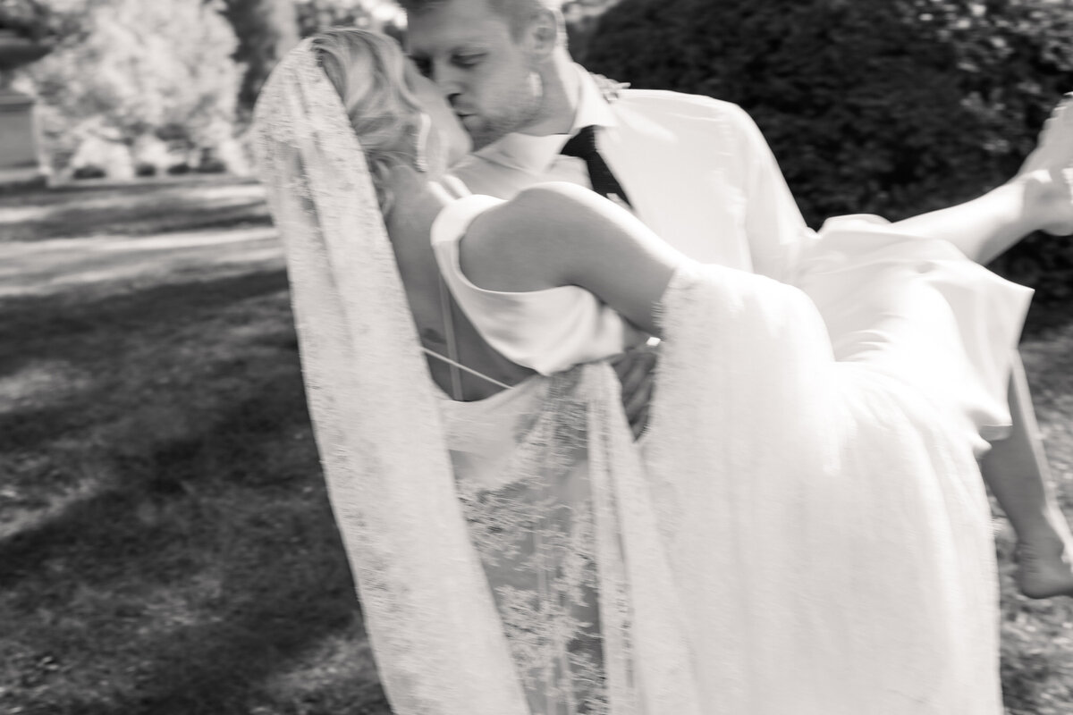 Groom carries bride while kissing her during sunny Dayton, Ohio wedding, shot by Philadelphia wedding photographer.