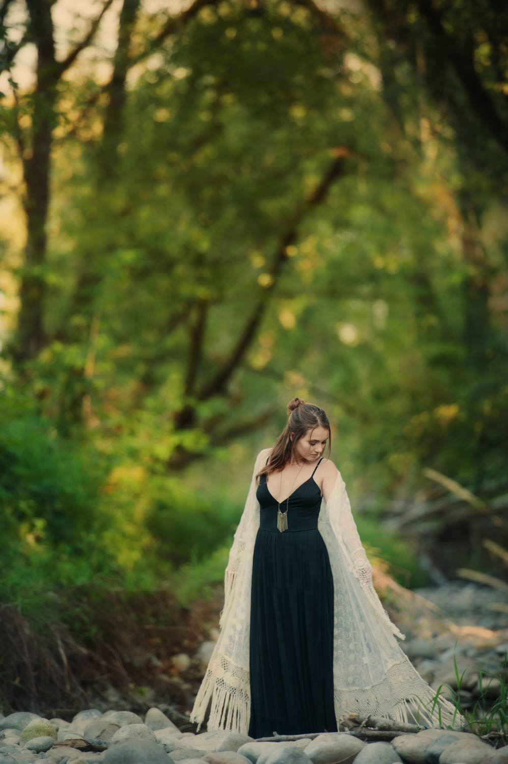 high school senior photo of girl in black dress and long cover in grove of trees