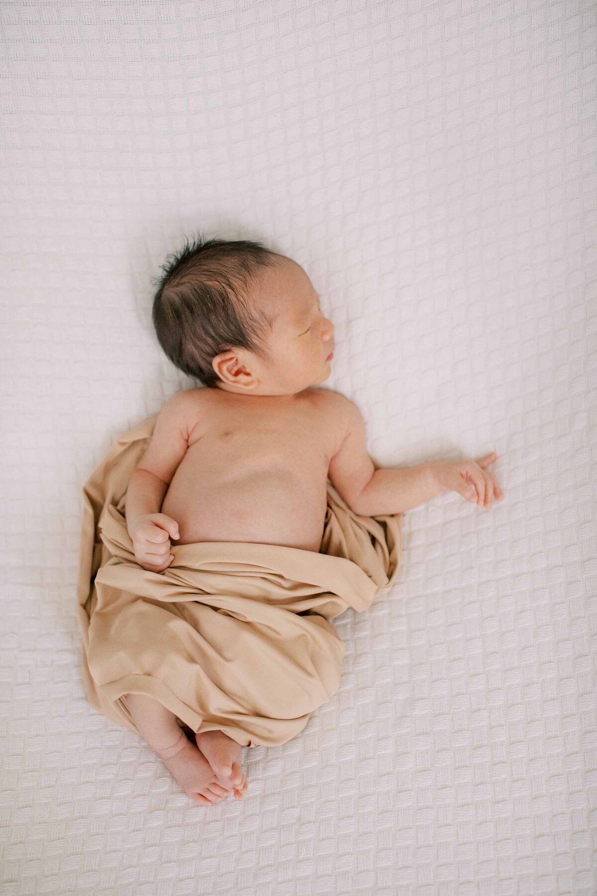 newborn baby boy wrapped in a neutral-colored swaddle and looking to the side