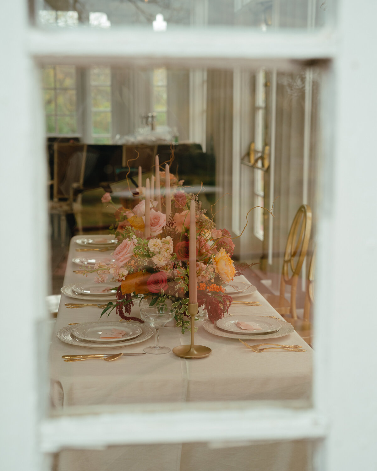 A table set with fine china and many pink and orange floral arrangements