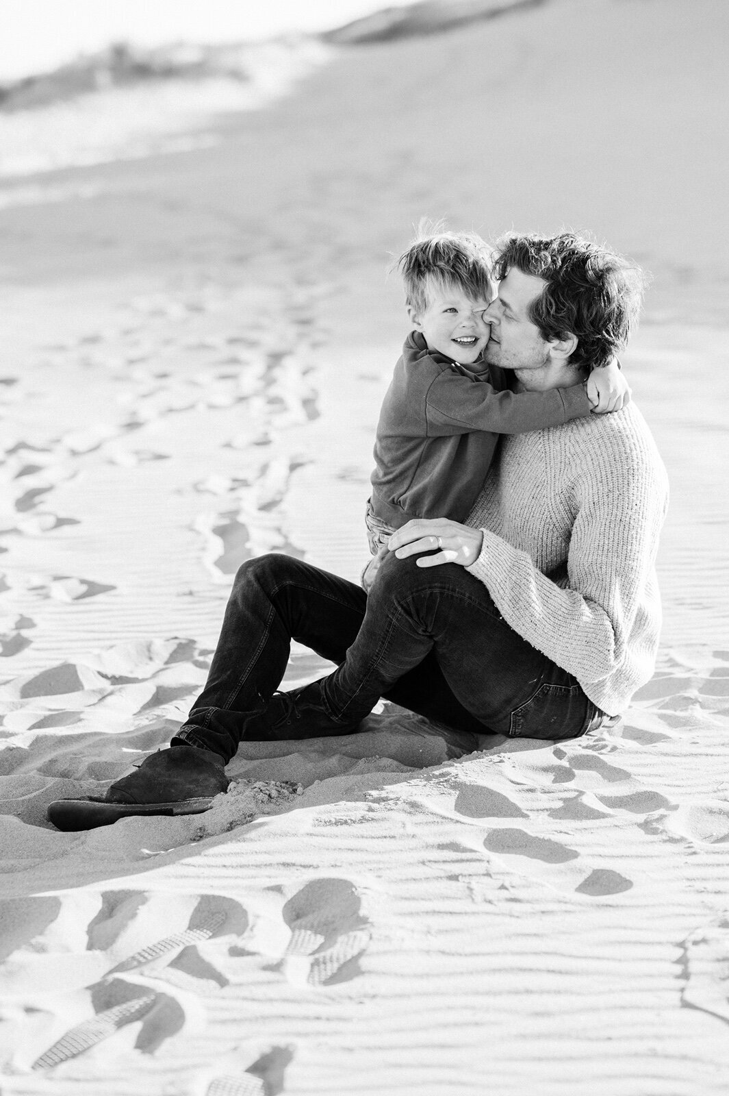 Vader en zoon zitten knuffelend op het strand