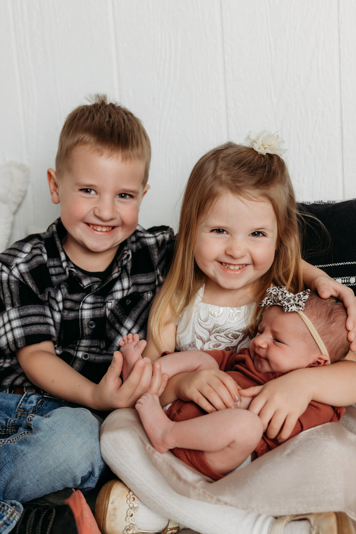 Smiling brother and sister cuddling their newborn sibling during a lifestyle newborn photo session with Mary Wiebe Photography in Lubbock, Texas.