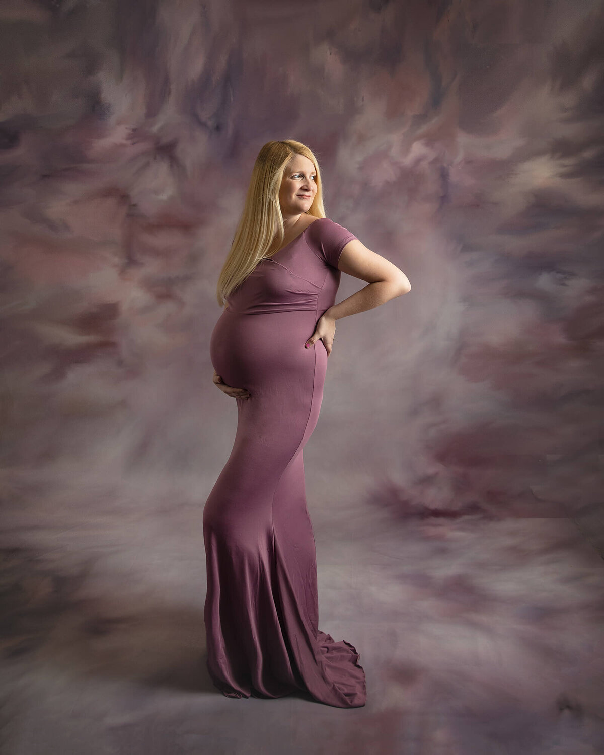 Pregnant woman looking over her shoulder wearing a purple maternity gown.