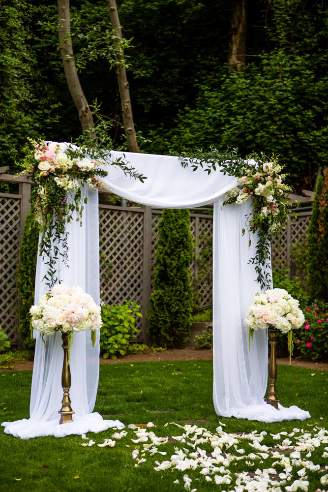 Romantic garden wedding ceremony white draped arch with greenery and peonies.