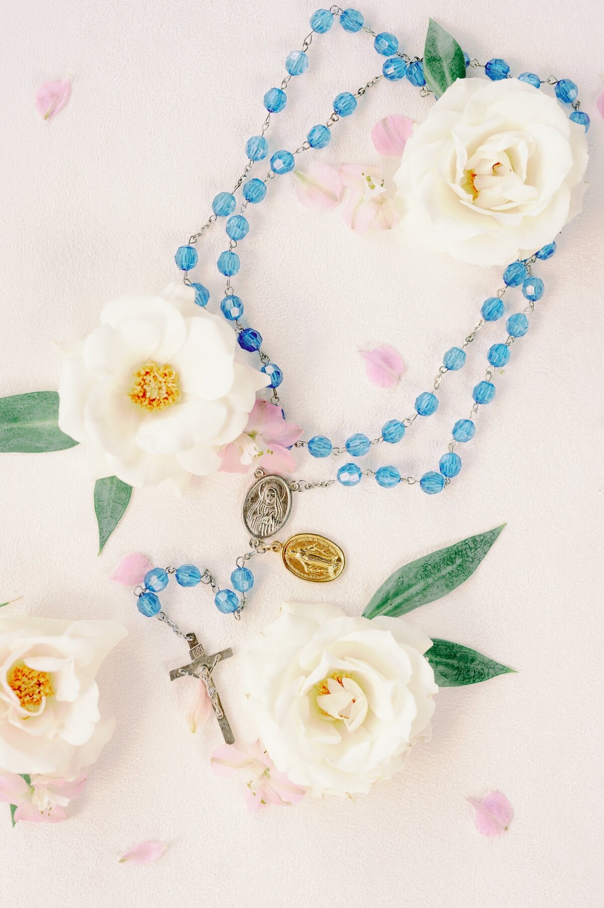 a flat lay of a Catholic rosary surrounded by wedding flowers