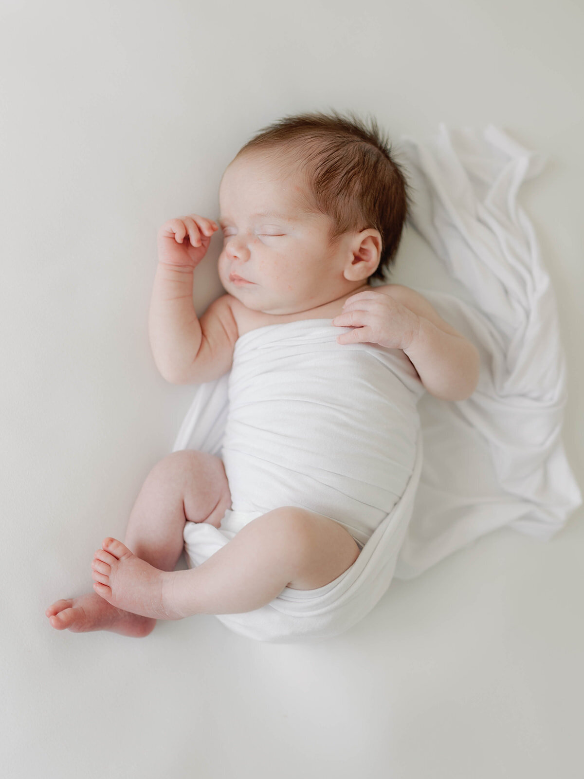 Newborn baby laying on back swaddled