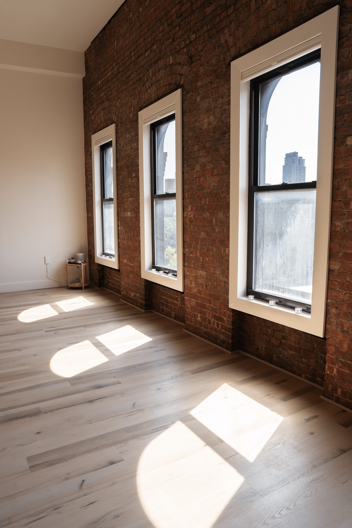 Bright, airy studio with brick walls, three large windows, and natural light streaming across wooden floors.