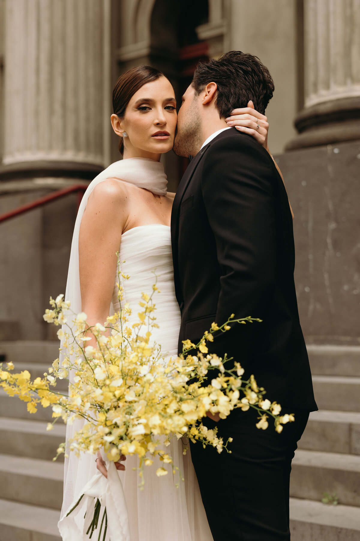 Bride holding yellow flowers while hugging groom