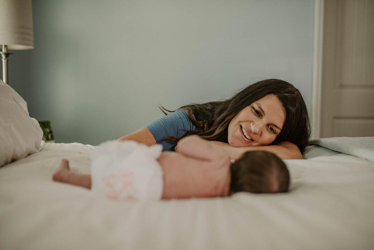 Mom smiles at baby on bed