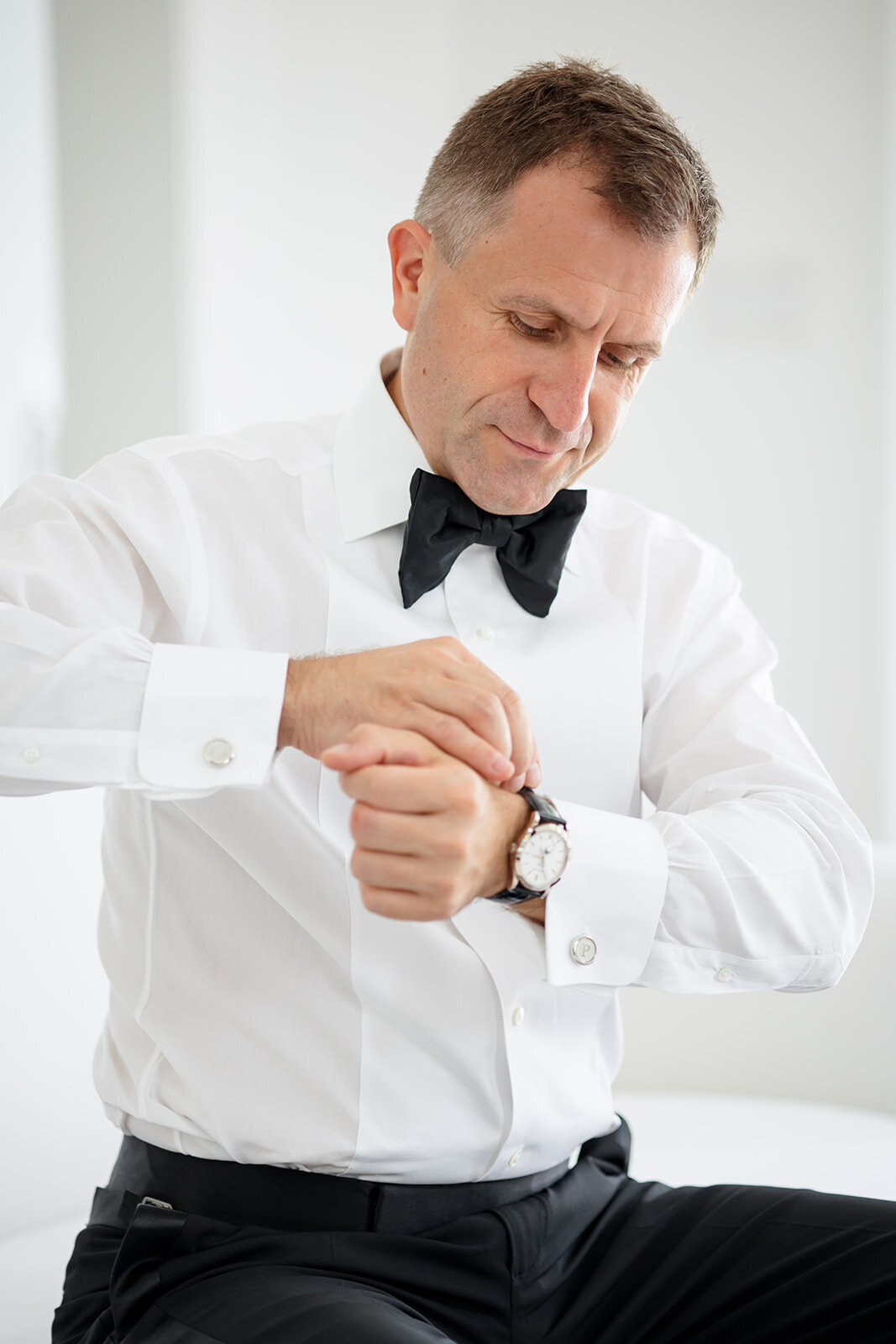 Groom adjusting his bow tie in a white shirt.
