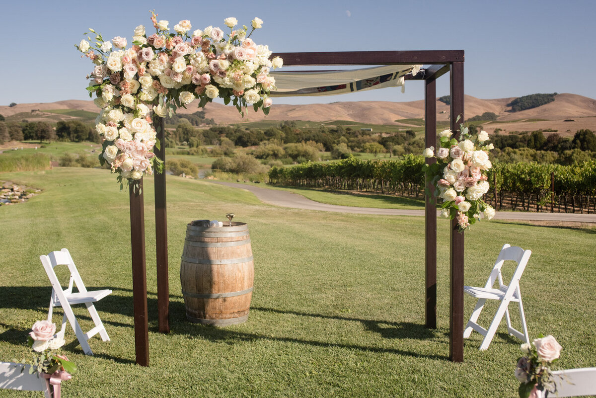 Vineyard wedding arch decorated with pink and white flowers overlooking hills