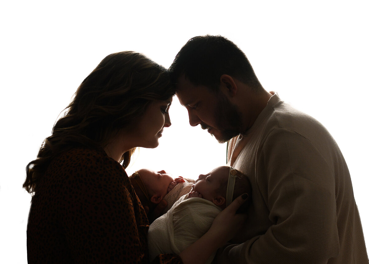 parents on white backlit background holding their baby girls