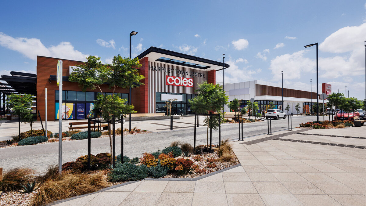Front facade of Coles at Harpley Town Centre, featuring landscaped pathways, trees, and a bold red-brick building with modern architectural lines.