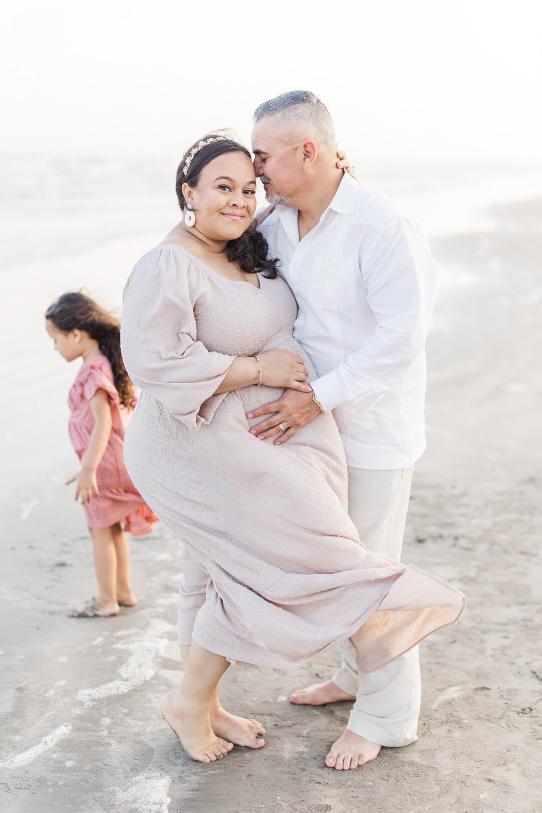 mom and dad embrace smiling holding pregnant belly for galveston maternity session