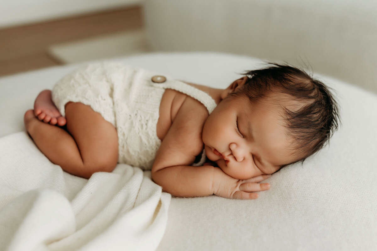 A newborn baby lays sleeping on a soft bed of blankets 