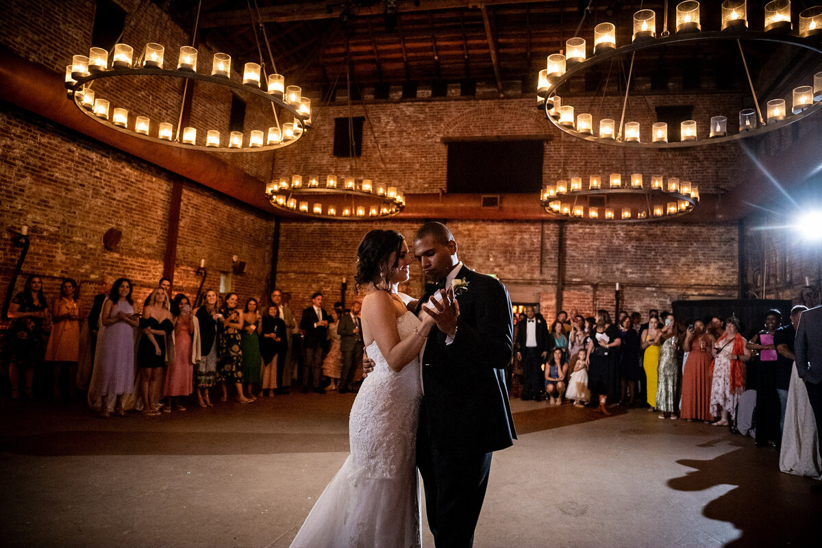 San Francisco Bay Area wedding photographer captures romantic first dance with dramatic circular lighting and stone walls surrounded by wedding guests at Estate Yountville in Napa Valley