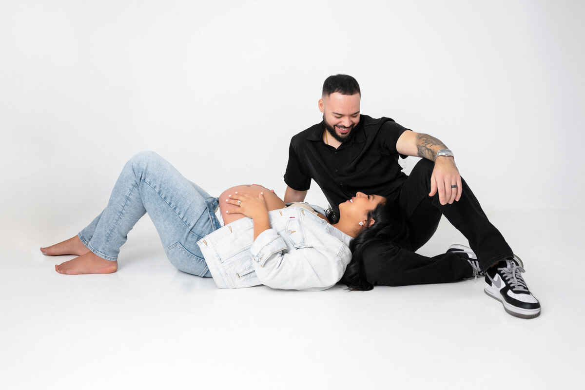 Pregnant mom lays on partner’s lap, gazing into each other’s eyes.