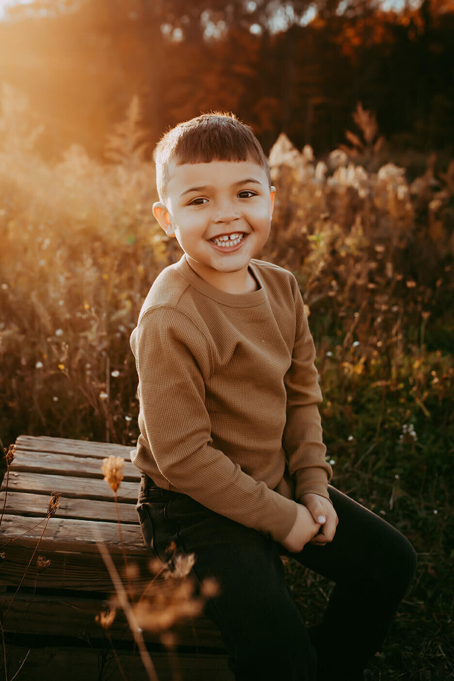 a five year old boy sitting on a wooden crate in a field during golden hour