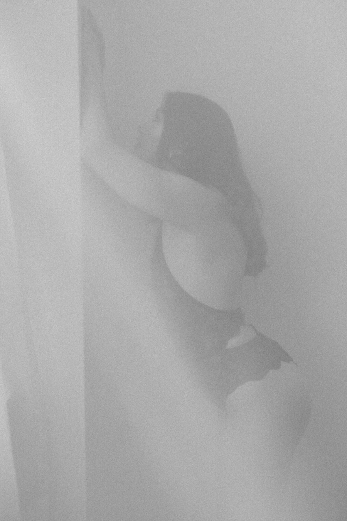 A boudoir photo shot through sheer curtains