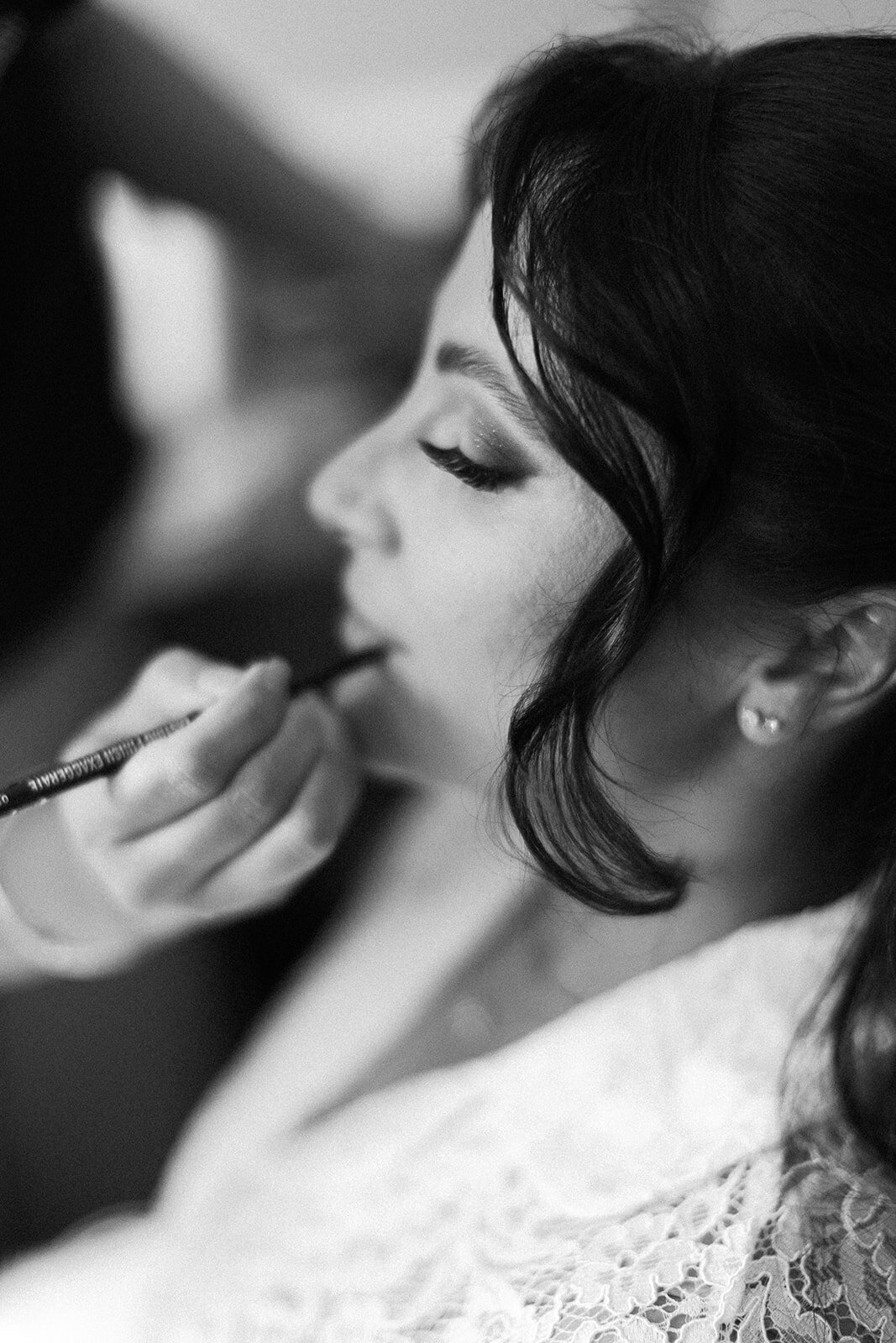 A black-and-white close-up of the bride as she gets her makeup done, highlighting her elegant lashes and serene expression, captured by Claudia Amalia Photography.
