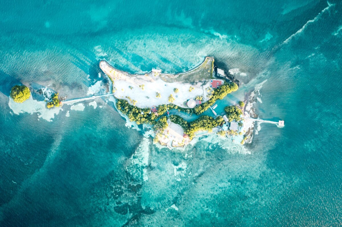 Aerial view of white sand island surrounded by light blue water in Royal, Belize