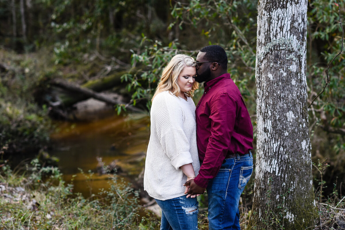 Beautiful Mississippi Engagement Photography: couple embraces on bank of a small creek in the woods in Mississippi