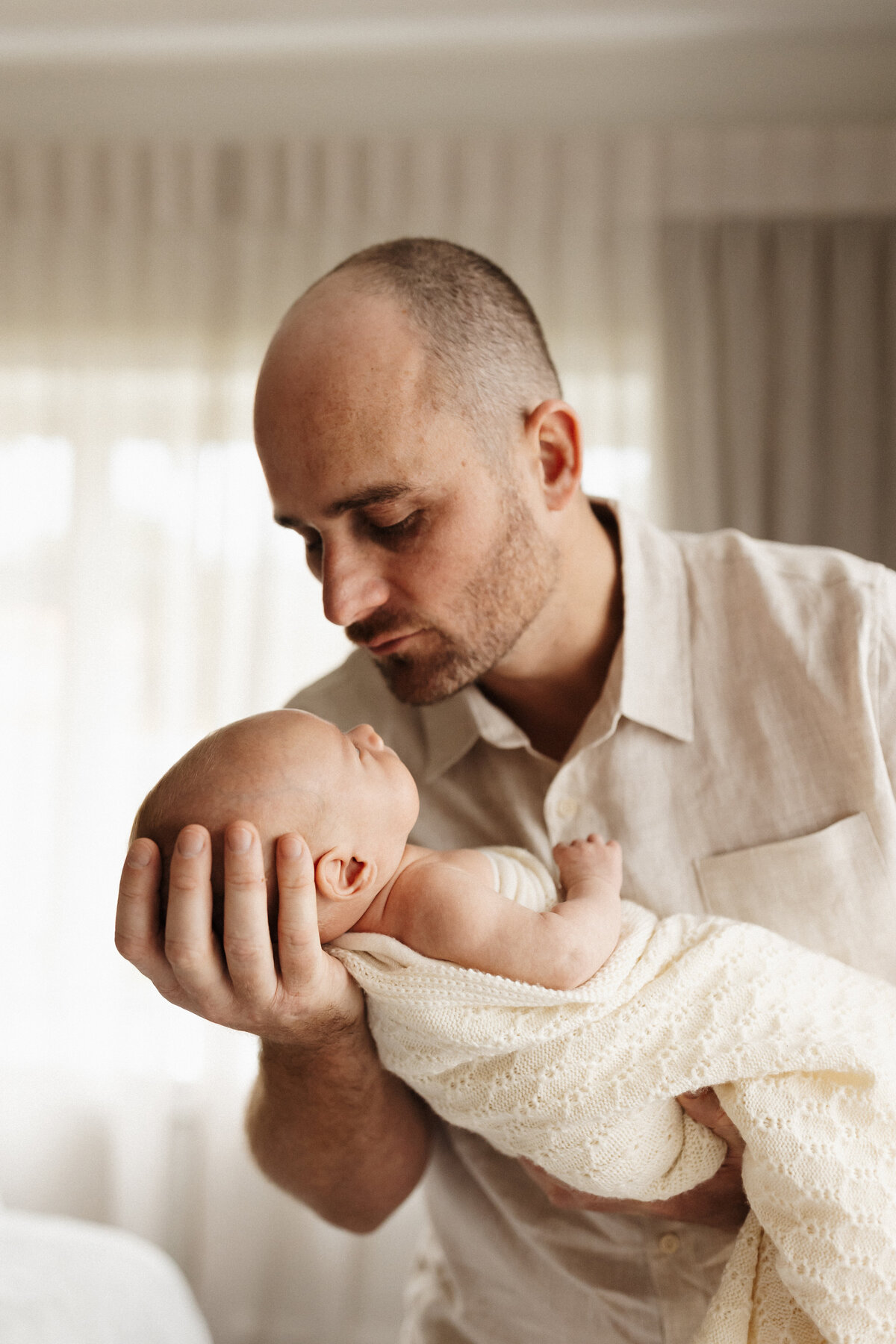 A father holding her newborn baby during a newborn in home family photoshoot with christchurch photographer lucy jane