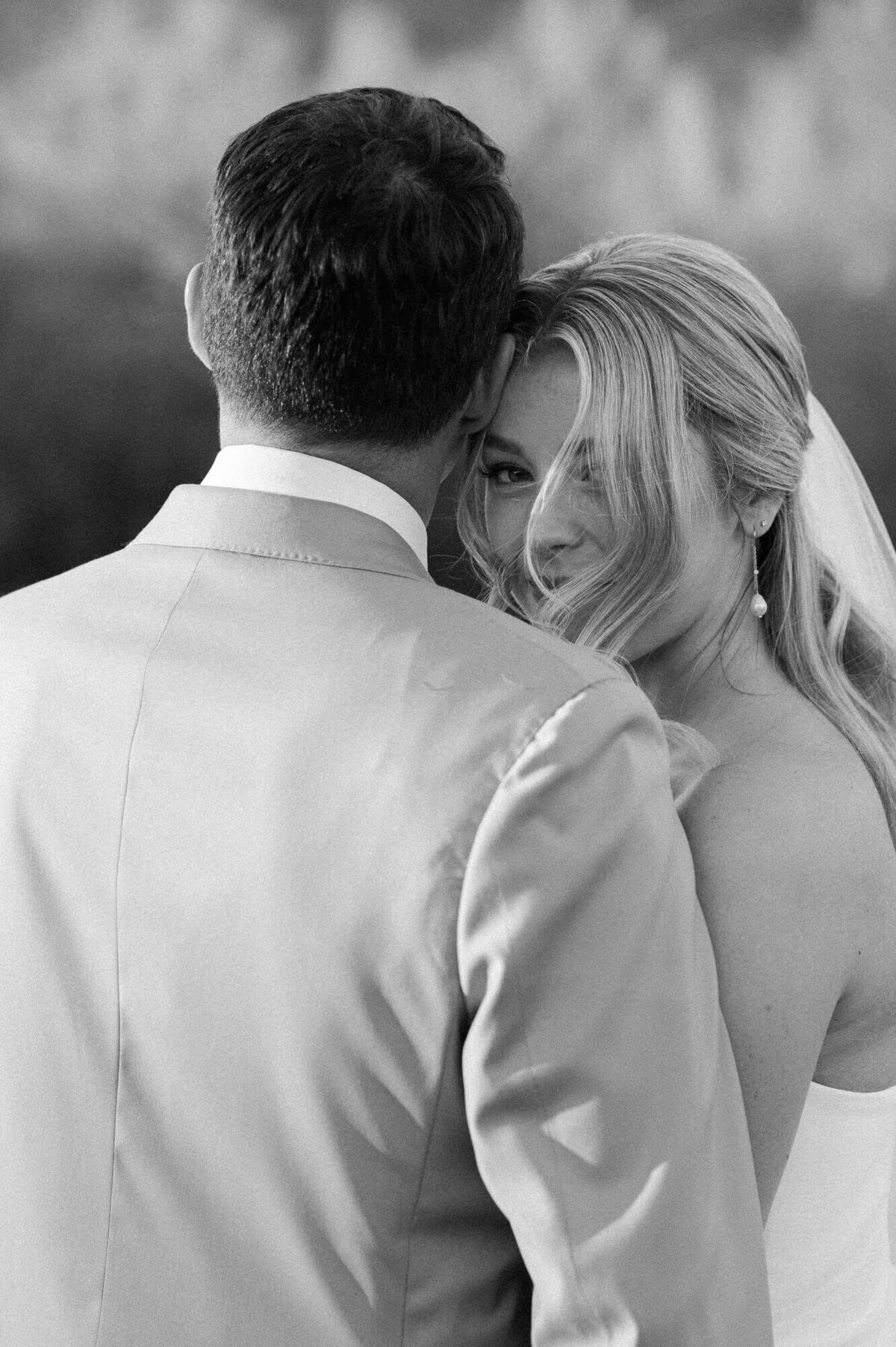 Bride smiling softly over her groom’s shoulder during golden hour portraits, captured by a wedding photographer in Arizona.