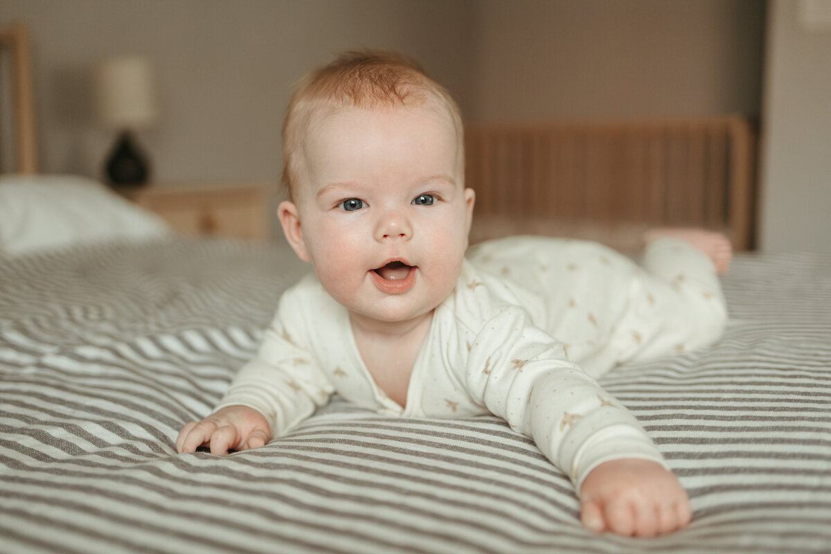 baby smiling while laying on belly on striped blanket during lifestyle in home session with alexis adkins photography in longmont colorado