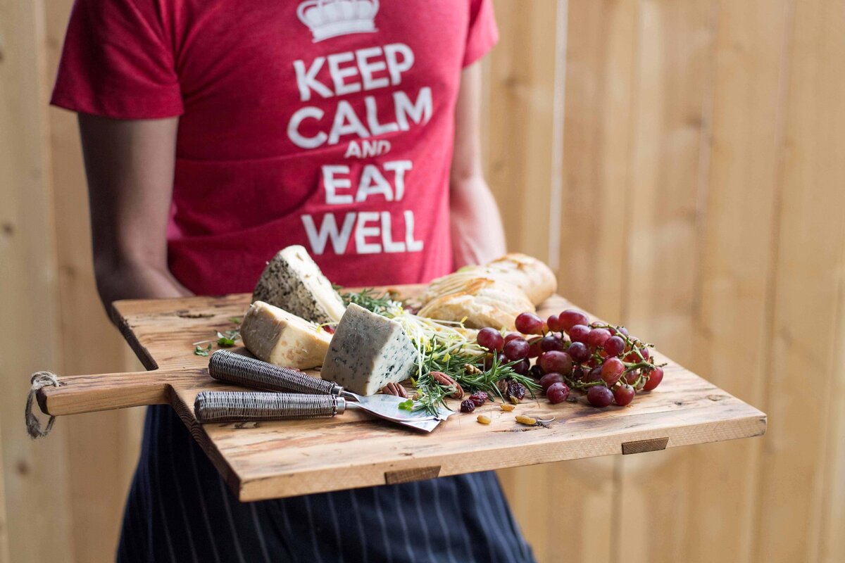 Artisen Cheese and graps being served on a rustic cutting board by waiter wearing "Keep Calm and Eat Well Shirt." Food marketing image.
