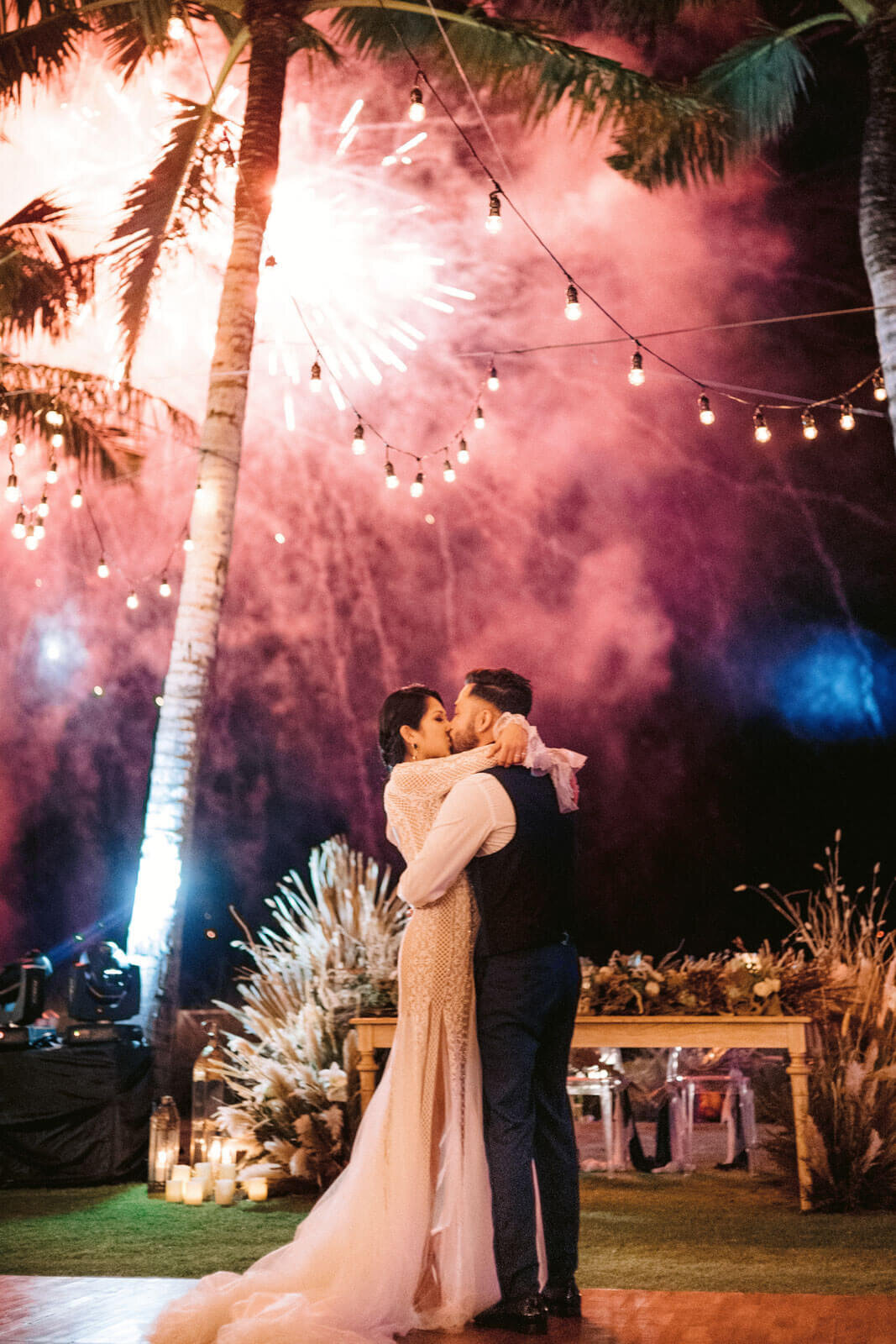 The bride and groom kiss in a wedding reception, with fireworks in the background in Bali, Indonesia. Image by Jenny Fu Studio