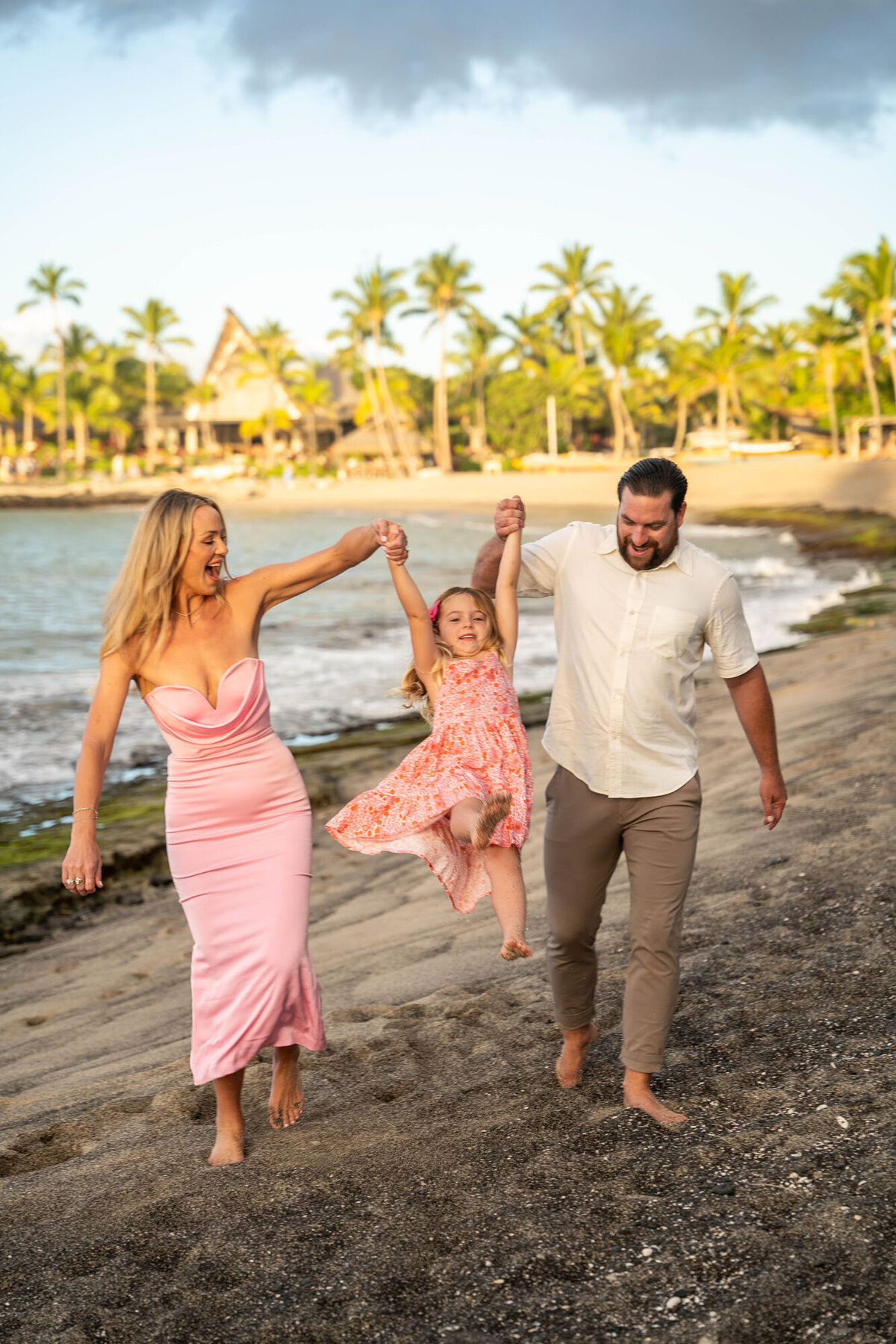Hawaii family portraits with parents swinging daughter on the beach